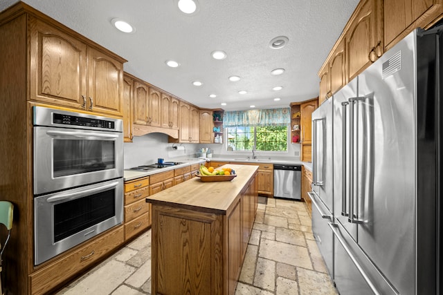 kitchen with appliances with stainless steel finishes, sink, a center island, butcher block countertops, and a textured ceiling