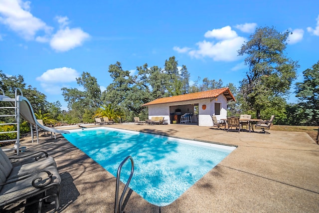 view of pool with a patio, a water slide, and a diving board