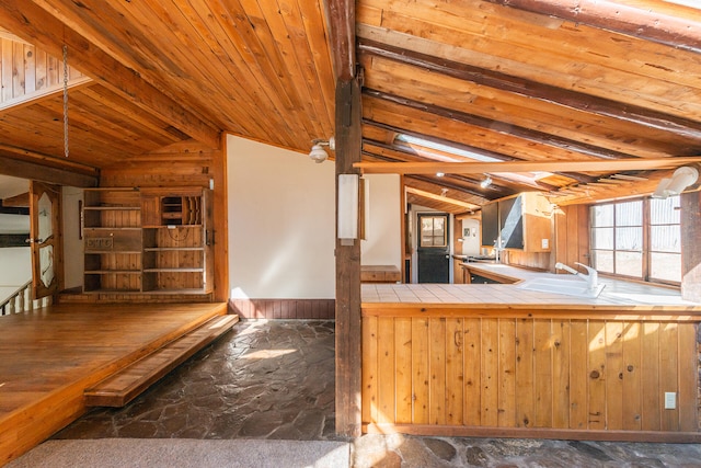 kitchen featuring wood ceiling, tile countertops, sink, lofted ceiling with beams, and wooden walls