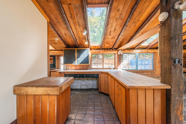 interior space with tile countertops, lofted ceiling with skylight, kitchen peninsula, and wooden ceiling