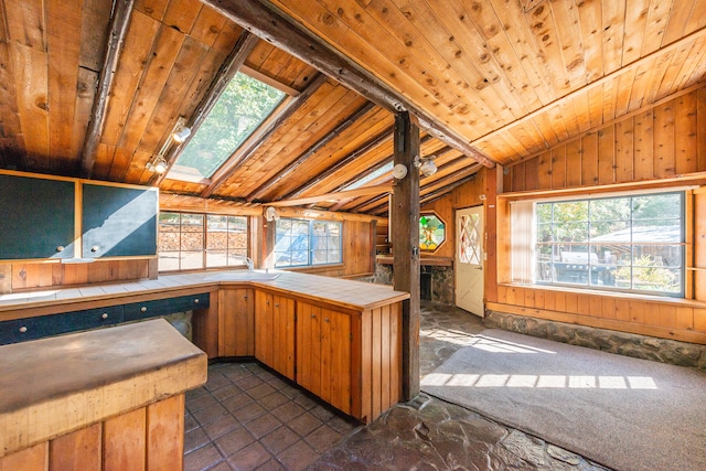 kitchen with vaulted ceiling with skylight, tile countertops, wooden walls, and wooden ceiling