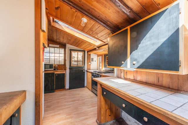 kitchen featuring tile countertops, wood ceiling, stainless steel appliances, lofted ceiling with skylight, and light hardwood / wood-style flooring