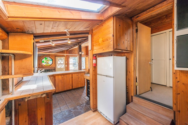 kitchen with lofted ceiling, tile countertops, light wood-type flooring, white refrigerator, and wood walls