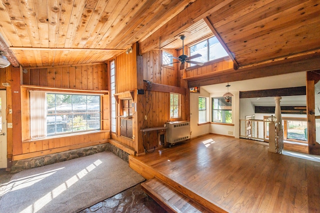 unfurnished living room featuring dark wood-type flooring, wooden walls, wooden ceiling, vaulted ceiling with skylight, and ceiling fan