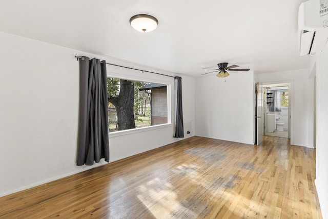 spare room featuring light hardwood / wood-style floors, an AC wall unit, ceiling fan, and a healthy amount of sunlight