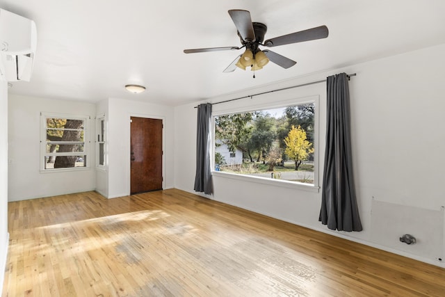 empty room with a wall mounted air conditioner, hardwood / wood-style flooring, a wealth of natural light, and ceiling fan