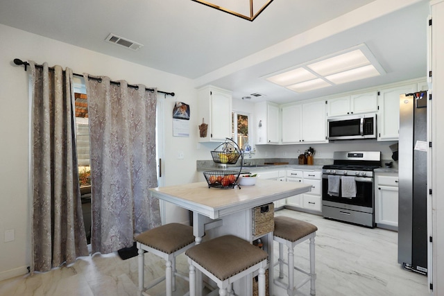 kitchen with a kitchen breakfast bar, white cabinets, and appliances with stainless steel finishes