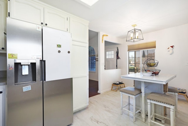 kitchen with hanging light fixtures, stainless steel refrigerator with ice dispenser, a kitchen breakfast bar, and white cabinetry