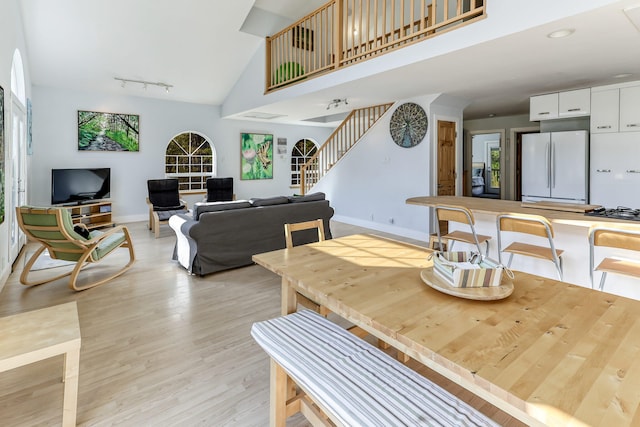 dining area with rail lighting, high vaulted ceiling, and light hardwood / wood-style floors