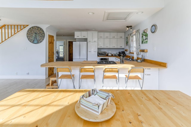 kitchen featuring kitchen peninsula, a breakfast bar, white refrigerator, white cabinets, and light hardwood / wood-style floors