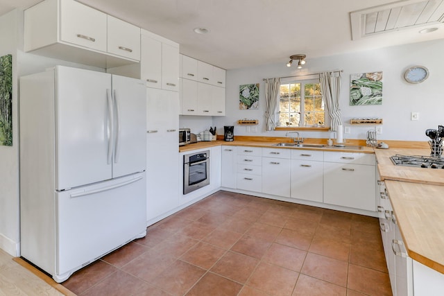 kitchen with appliances with stainless steel finishes, light tile patterned flooring, white cabinets, and butcher block counters