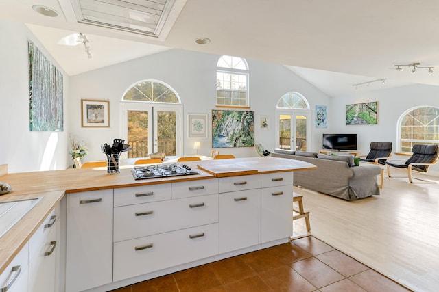 kitchen with vaulted ceiling, white cabinets, light tile patterned floors, and wood counters