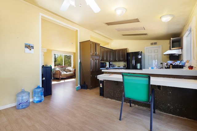 kitchen with light wood-type flooring, dark brown cabinets, kitchen peninsula, black fridge, and lofted ceiling