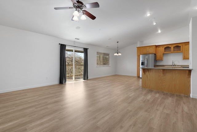 unfurnished living room with lofted ceiling, sink, ceiling fan with notable chandelier, and light wood-type flooring