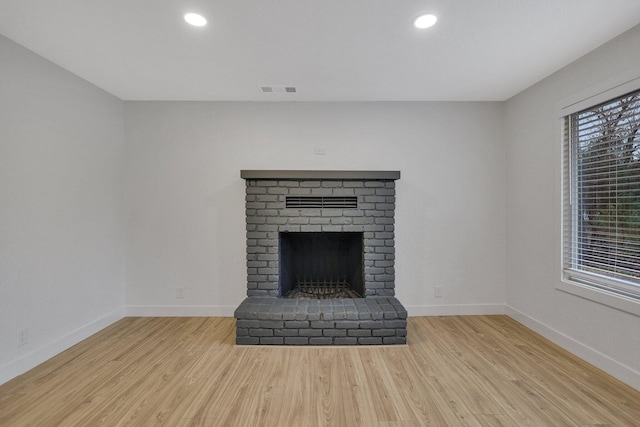 unfurnished living room featuring a brick fireplace and light hardwood / wood-style flooring