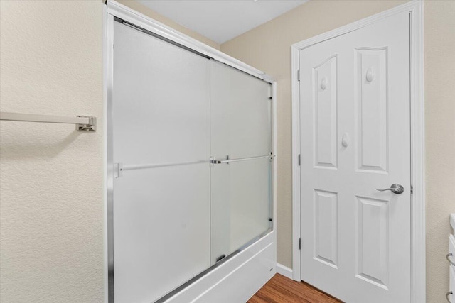 bathroom with combined bath / shower with glass door and wood-type flooring