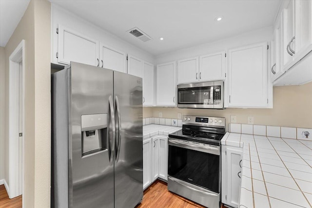 kitchen with tile countertops, white cabinetry, stainless steel appliances, and light wood-type flooring