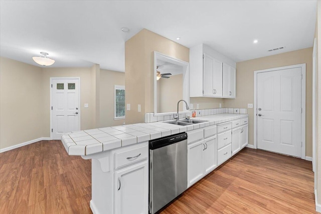 kitchen with stainless steel dishwasher, white cabinets, kitchen peninsula, and tile counters