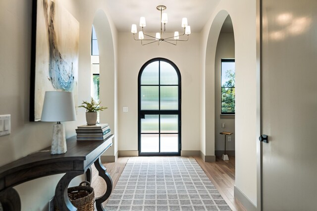doorway to outside with a chandelier, arched walkways, light wood-style floors, and baseboards