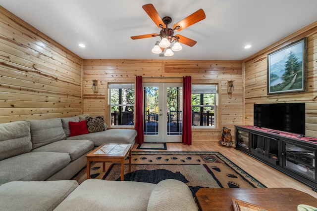 living room featuring wooden walls, hardwood / wood-style floors, ceiling fan, and french doors