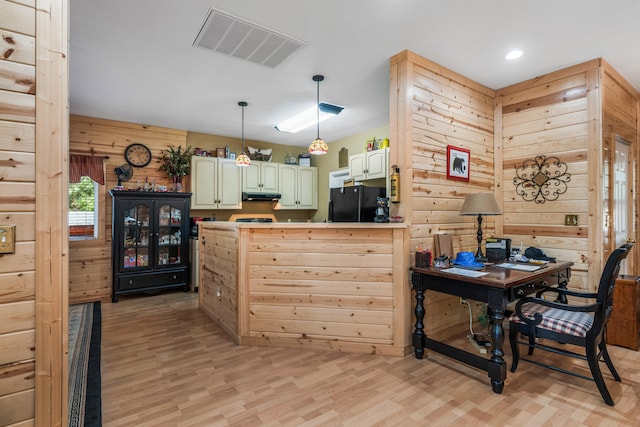 kitchen with black fridge, wooden walls, light wood-type flooring, decorative light fixtures, and kitchen peninsula