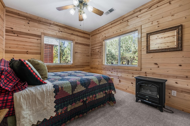 carpeted bedroom featuring ceiling fan, wood walls, and a wood stove