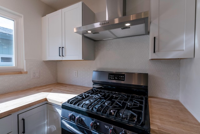 kitchen with wall chimney range hood, butcher block counters, a healthy amount of sunlight, and gas range