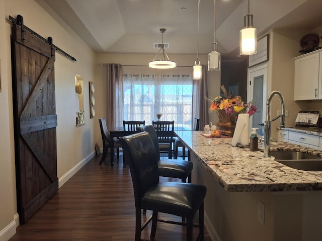 kitchen with light stone countertops, white cabinetry, sink, hanging light fixtures, and a barn door