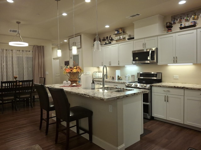 kitchen featuring white cabinets, decorative light fixtures, stainless steel appliances, and an island with sink