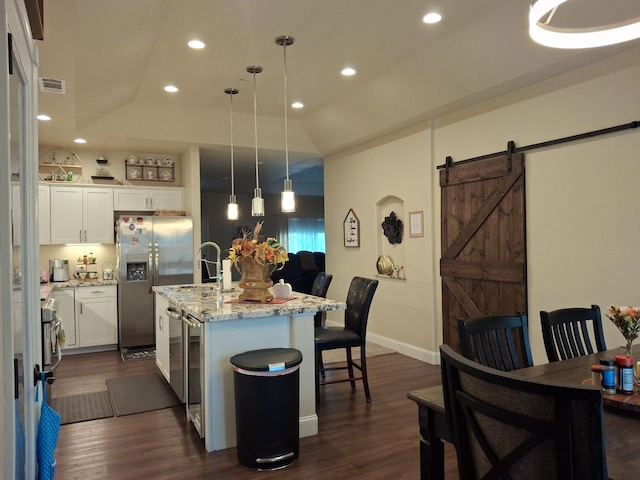 kitchen with white cabinets, a barn door, hanging light fixtures, and an island with sink