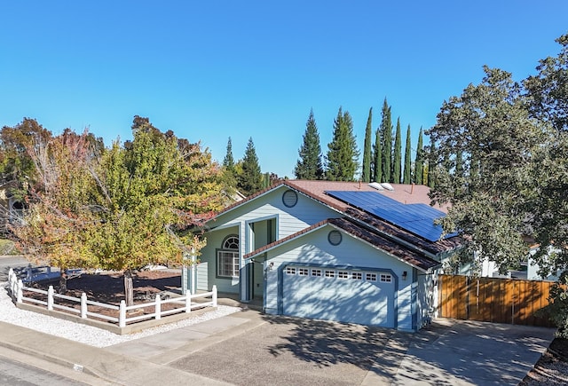 view of front of property with an attached garage, driveway, a fenced front yard, and solar panels