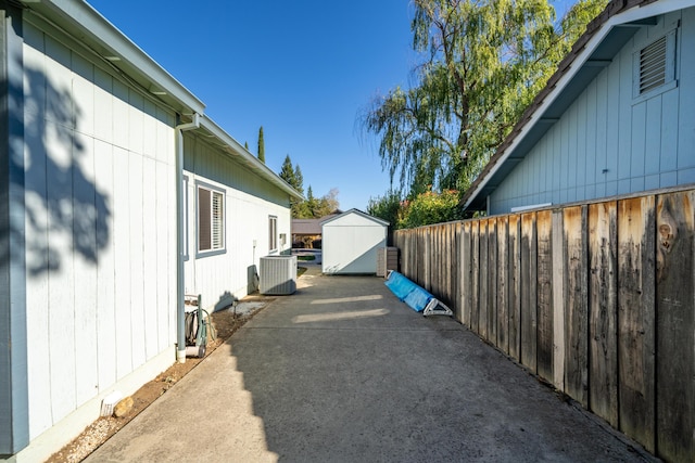 view of patio featuring central air condition unit, an outdoor structure, a storage unit, and fence