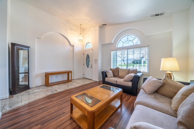 living area with a towering ceiling, baseboards, visible vents, and wood finished floors