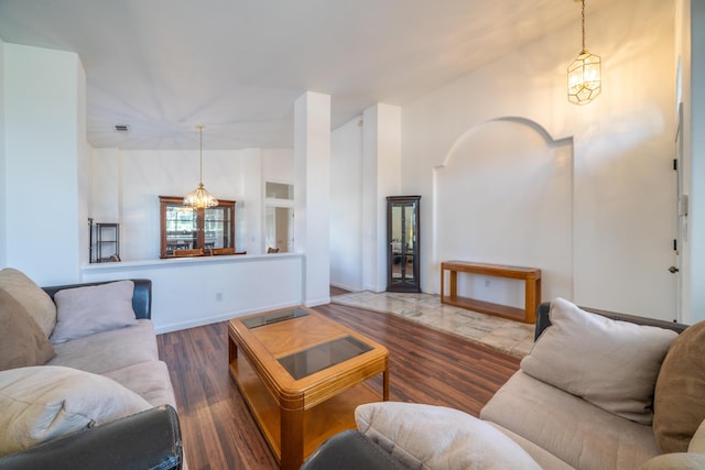 living area featuring baseboards, visible vents, lofted ceiling, wood finished floors, and a notable chandelier