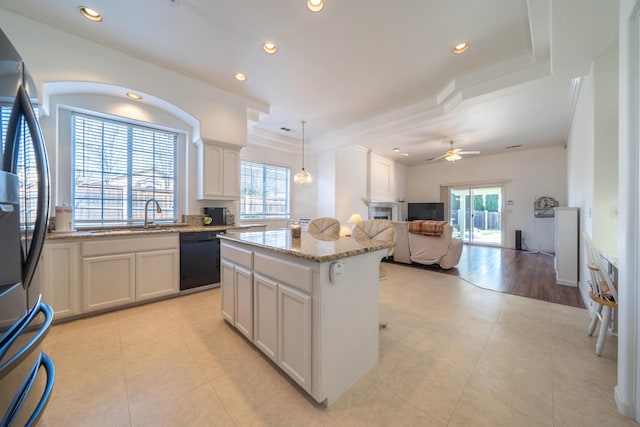 kitchen featuring decorative light fixtures, open floor plan, a kitchen island, light stone countertops, and dishwasher