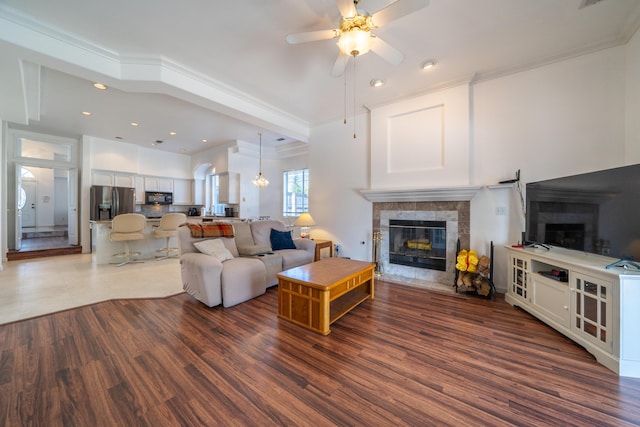 living area with recessed lighting, a tiled fireplace, ornamental molding, ceiling fan, and wood finished floors