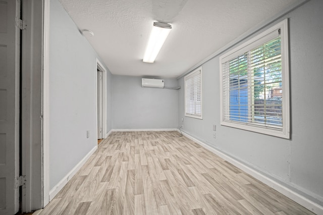 basement featuring a wall unit AC, a textured ceiling, and light wood-type flooring