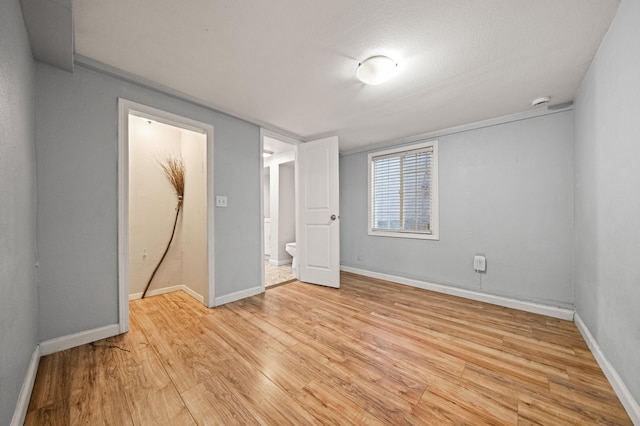 unfurnished bedroom with ensuite bathroom, light wood-type flooring, and a textured ceiling