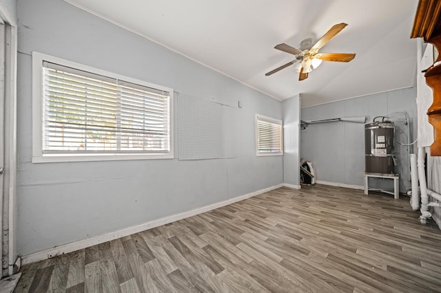 unfurnished room with secured water heater, ceiling fan, hardwood / wood-style floors, and vaulted ceiling