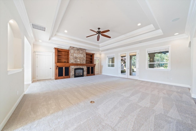 unfurnished living room with a stone fireplace, light carpet, crown molding, and a raised ceiling