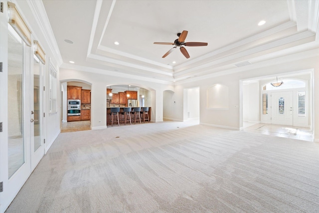 unfurnished living room featuring a tray ceiling, light colored carpet, and ornamental molding