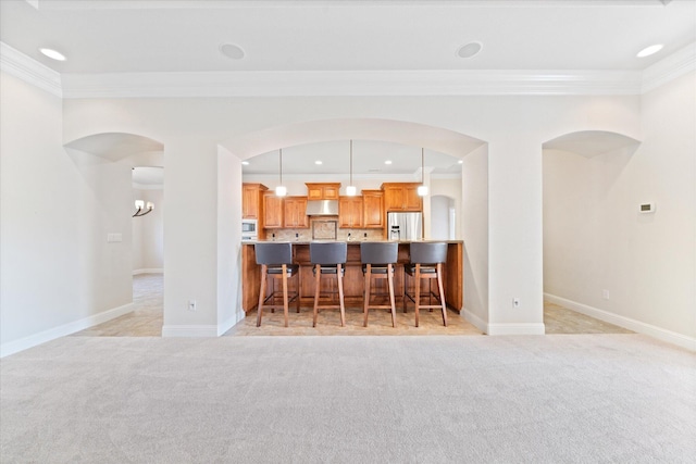 kitchen featuring crown molding, appliances with stainless steel finishes, light carpet, and decorative light fixtures