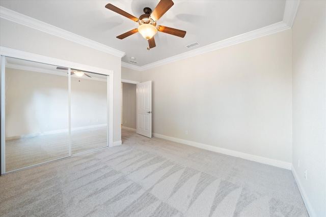 unfurnished bedroom with a closet, light colored carpet, ceiling fan, and crown molding