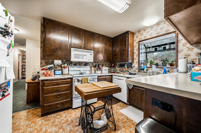 kitchen with dark brown cabinetry, light colored carpet, and white appliances