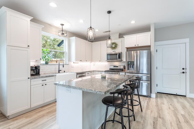 kitchen with appliances with stainless steel finishes, a center island, pendant lighting, white cabinets, and light stone counters