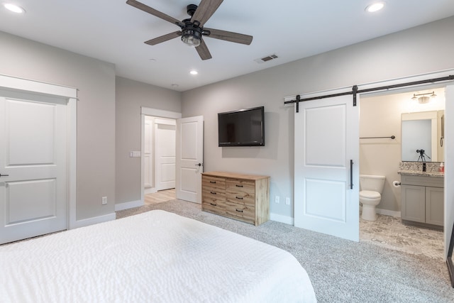 bedroom with light colored carpet, ceiling fan, ensuite bathroom, and a barn door