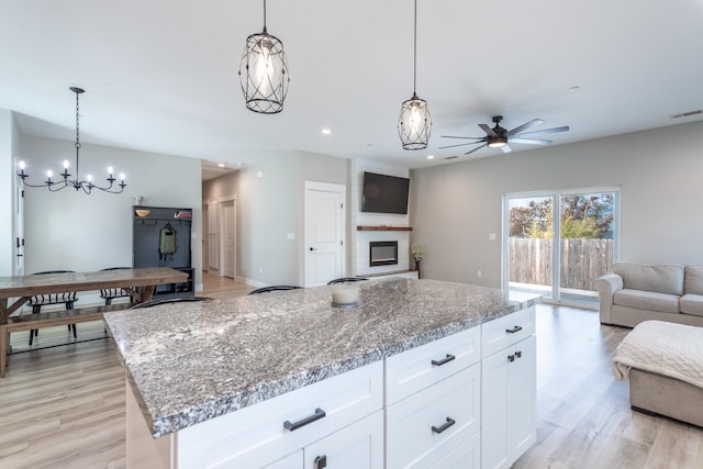 kitchen with hanging light fixtures, a kitchen island, white cabinetry, light stone countertops, and light hardwood / wood-style flooring