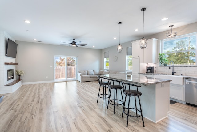 kitchen featuring dishwasher, light wood-type flooring, stone countertops, a center island, and white cabinets