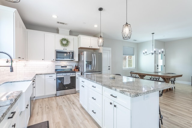 kitchen featuring appliances with stainless steel finishes, a kitchen island, decorative light fixtures, white cabinets, and light hardwood / wood-style flooring