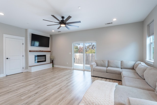 unfurnished living room with a large fireplace, light wood-type flooring, and ceiling fan